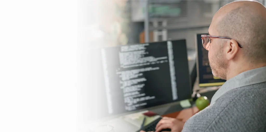 IT specialist with glasses reviewing code on a monitor, cybersecurity services in Atlanta