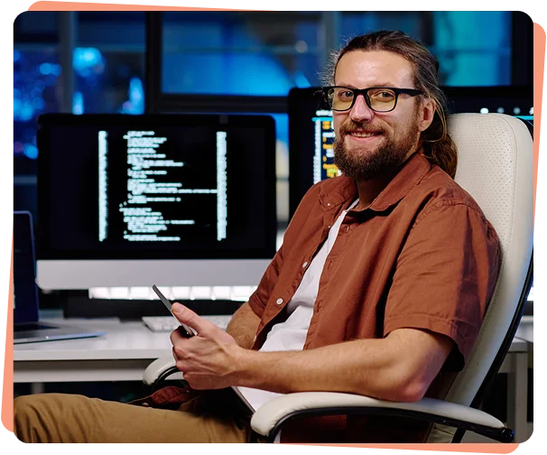 Smiling developer with a phone in front of monitors showing code, cybersecurity services Tampa