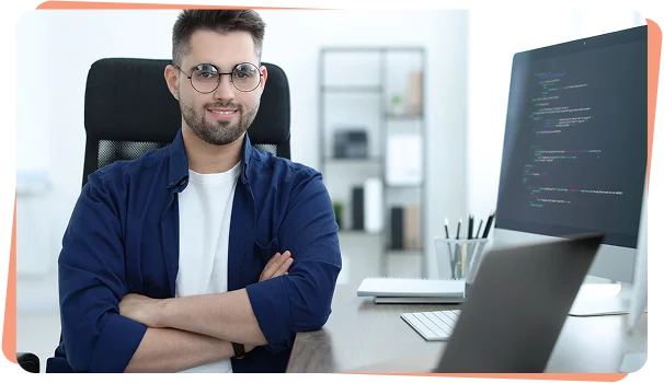 Confident developer with arms crossed beside a monitor showing code, cybersecurity services NYC