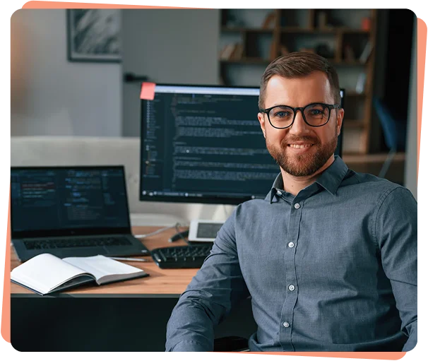 Smiling developer with glasses at a desk with code on screen, cybersecurity services Denver