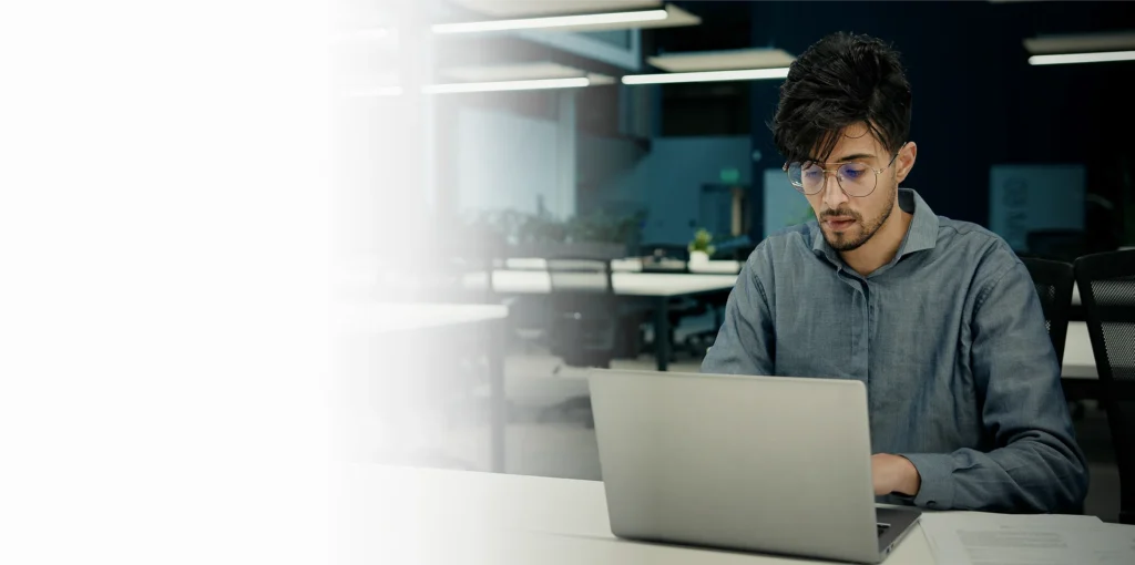 Engineer working on a laptop in a dimly lit office, OT cybersecurity services