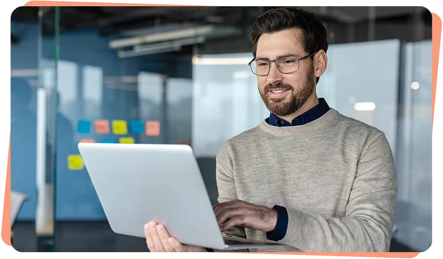 Smiling engineer with glasses holding a laptop in an office, operational technology cybersecurity