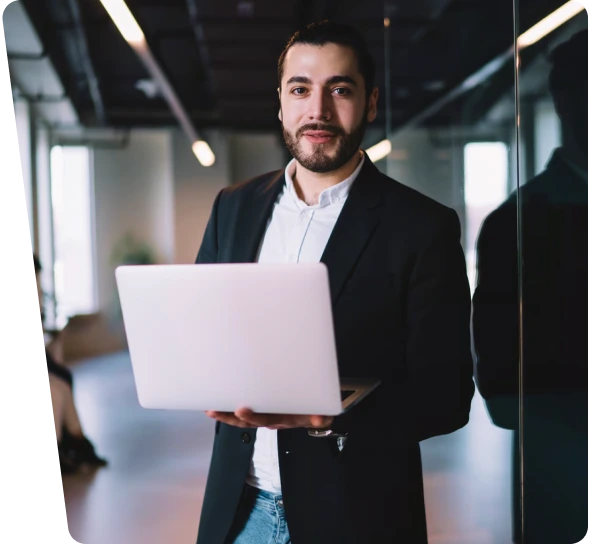 Smiling professional holding a laptop in a modern office, OT cybersecurity services
